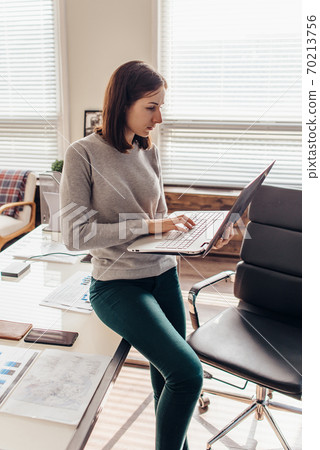 woman standing typing on a notebook keyboard in her office 70213756