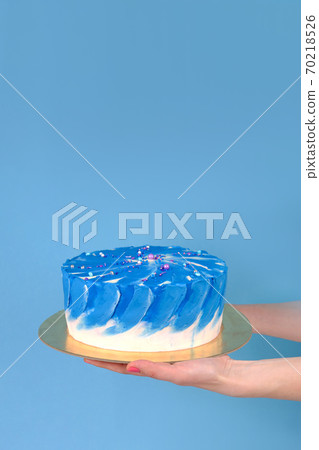 Girl's hands are holding beautiful and tasty cake with white and true blue color cream on a blue background with place for text. 70218526