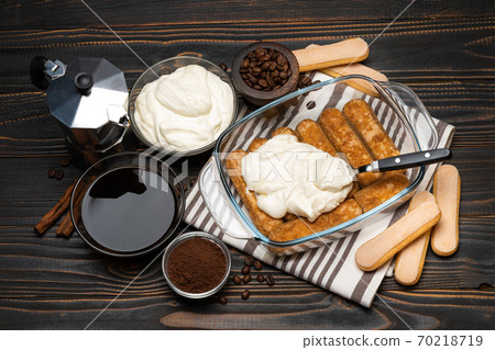 tiramisu dessert cooking - Traditional Italian Savoiardi ladyfingers Biscuits and cream in glass baking dish, coffee maker on wooden background tiramisu dessert cooking - Traditional Italian Savoiardi ladyfingers Biscuits and cream in glass baking dish, coffee maker on wooden background 70218719