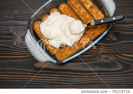 tiramisu dessert cooking - Traditional Italian Savoiardi ladyfingers Biscuits and cream in glass baking dish on wooden background tiramisu dessert cooking - Traditional Italian Savoiardi ladyfingers Biscuits and cream in glass baking dish on wooden background 70218738