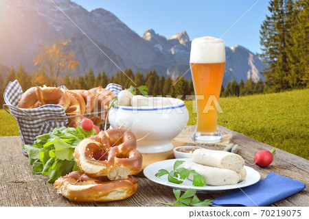 Bavarian breakfast with Munich veal sausages, fresh pretzels and a wheat beer outside in the nature Bavarian breakfast with Munich veal sausages, fresh pretzels and a wheat beer outside in the nature 70219075