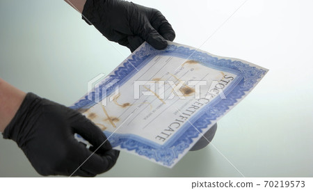 Close up hands hold stock certificate damaged by fire. Close up hands hold stock certificate damaged by fire. 70219573