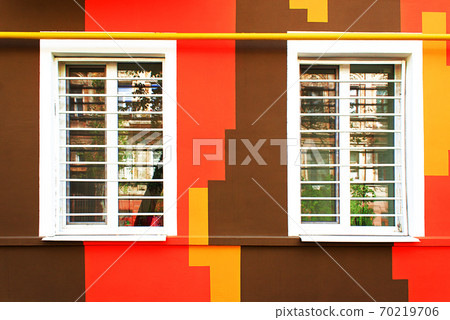 Two white windows on the background of a colored wall. The colored wall of the house is painted yellow, brown, orange 70219706