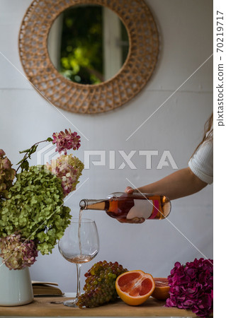 Bath tub with flower petals, grapefruit slices, bunch of grapes and woman's hand holding a bottle of wine 70219717