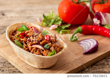 Mexican barquita taco with beef, chilli, tomato, onion and spices on wooden table 70219831