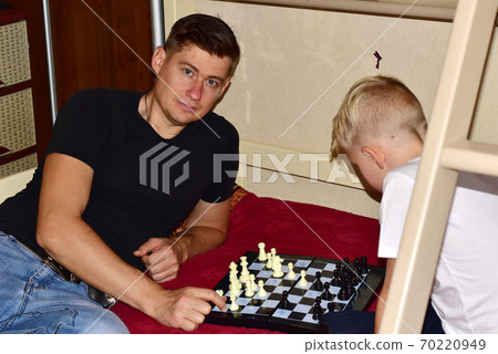 Boy and dad are playing chess on the bed in the room. Boy and dad are playing chess on the bed in the room. 70220949