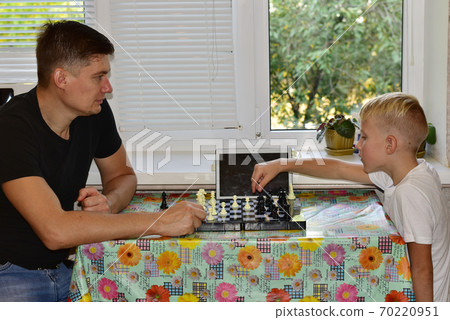 Father and son play chess at the table in front of the window. Father and son play chess at the table in front of the window. 70220951