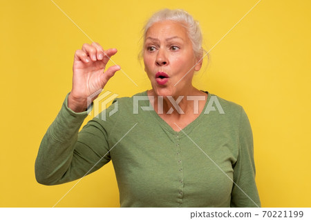 Surprised senior woman shows something small with hands Surprised senior woman shows something small with hands 70221199