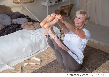 Active senior woman doing yoga training at home, holding navasana or boat yoga pose 70221510