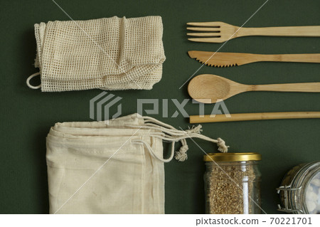 Zero waste kit. Set of eco friendly bamboo cutlery, mesh cotton bags, glass jars with a nuts. Plastic free lifestyle concept. Natural and reusable items accessories on green surface. 70221701