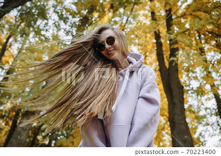 Young woman wearing pink hoodie and jeaans having fun in the park at sunny autumn day. Season and people concept. Young woman wearing pink hoodie and jeaans having fun in the park at sunny autumn day. Season and people concept. 70223400
