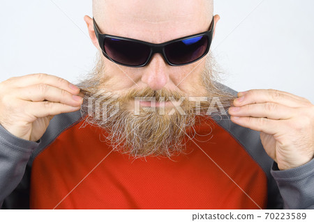 Portrait of a bald, bearded man wearing dark glasses on a light background 70223589