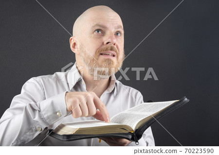 bearded man reading the Bible points his finger at the text and looks up 70223590