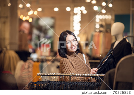 A young smiling girl shopping for clothes in a city mall, lookin A young smiling girl shopping for clothes in a city mall, lookin 70226838