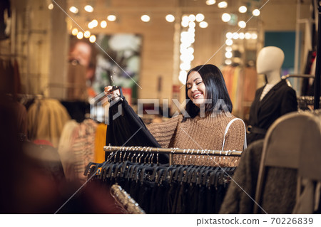 Young smiling girl looking for the right skirt in a shopping mal 70226839