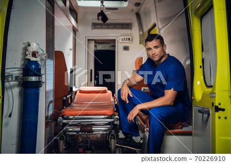 Paramedic in a blue medical uniform sitting in an ambulance car Paramedic in a blue medical uniform sitting in an ambulance car 70226910