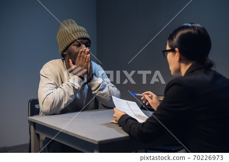 A lawyer girl with glasses and a young black guy communicate in the interrogation room about the grounds for his detention 70226973