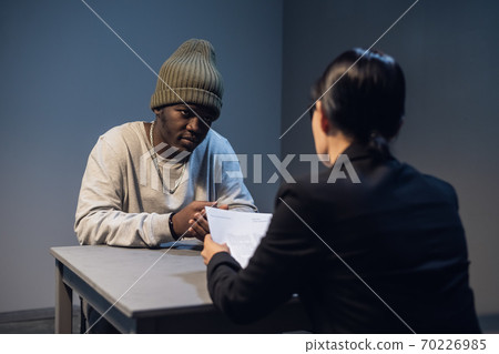 A lawyer girl with glasses and a young black guy communicate in the interrogation room about the grounds for his detention A lawyer girl with glasses and a young black guy communicate in the interrogation room about the grounds for his detention 70226985