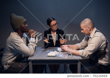 A drug dealer detained with a package containing an unknown white substance is interrogated by an experienced investigator in the presence of a lawyer A drug dealer detained with a package containing an unknown white substance is interrogated by an experienced investigator in the presence of a lawyer 70226988