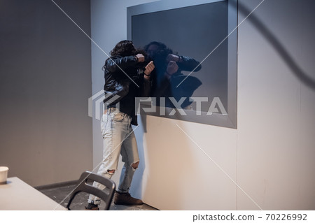 A white man with tattoos on his face tries to break the Gesell mirror in the police station interview room, because he is innocent of the crime he is accused of. 70226992