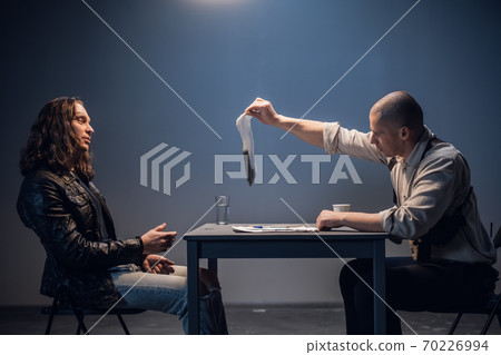A bald strong police investigator presents evidence to the accused in the case of illegal distribution and storage of weapons in the police station. 70226994