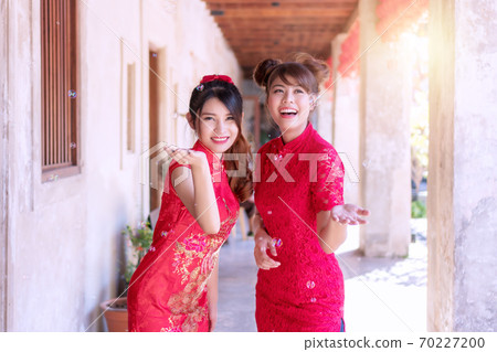 Cheerful beautiful smile two young woman friend wear cheongsam red dress holding hands Cheerful beautiful smile two young woman friend wear cheongsam red dress holding hands 70227200