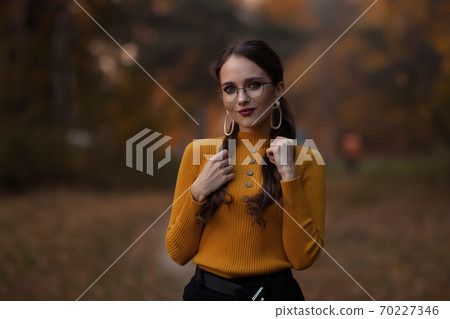 Charming young woman standing in autumnal park Charming young woman standing in autumnal park 70227346