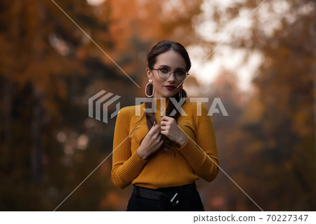 Charming young woman standing in autumnal park Charming young woman standing in autumnal park 70227347