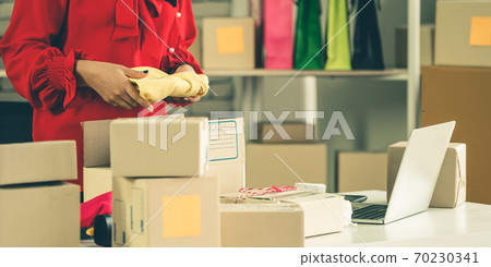 Online seller works at home office and packs shipping delivery box to customer. Online seller works at home office and packs shipping delivery box to customer. 70230341