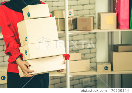 Online seller works at home office and packs shipping delivery box to customer. Online seller works at home office and packs shipping delivery box to customer. 70230344