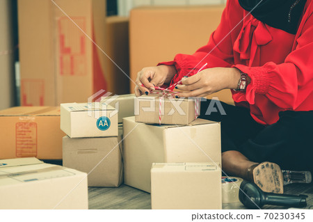 Online seller works at home office and packs shipping delivery box to customer. Online seller works at home office and packs shipping delivery box to customer. 70230345