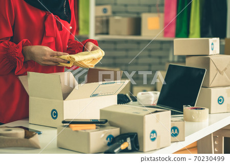 Online seller works at home office and packs shipping delivery box to customer. Online seller works at home office and packs shipping delivery box to customer. 70230499