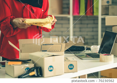 Online seller works at home office and packs shipping delivery box to customer. Online seller works at home office and packs shipping delivery box to customer. 70230562