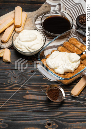 tiramisu dessert cooking - Traditional Italian Savoiardi ladyfingers Biscuits and cream in glass baking dish and coffee on wooden background tiramisu dessert cooking - Traditional Italian Savoiardi ladyfingers Biscuits and cream in glass baking dish and coffee on wooden background 70231104