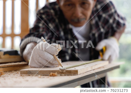 Close up senior man use tape measure to measure width of wood plank in carpentry workshop. 70231273