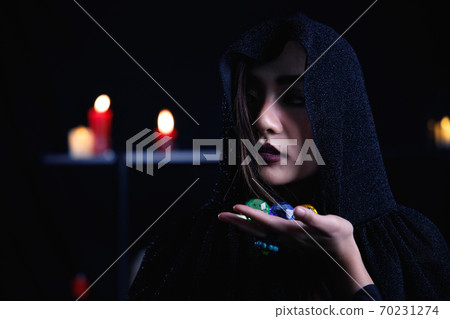Mystery woman in black hood hold colorful gem on dark background. 70231274