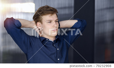 Young blond businessman and programmer stretching hands after working hard with computer in a darkened office, glare of light on the background Young blond businessman and programmer stretching hands after working hard with computer in a darkened office, glare of light on the background 70232908