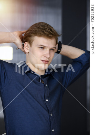 Young blond businessman and programmer stretching hands after working hard with computer in a darkened office, glare of light on the background Young blond businessman and programmer stretching hands after working hard with computer in a darkened office, glare of light on the background 70232938