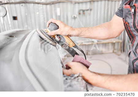 The mechanic works with a grinding tool. Sanding of car elements. Garage painting car service. Repairing car section after the accident. 70235470