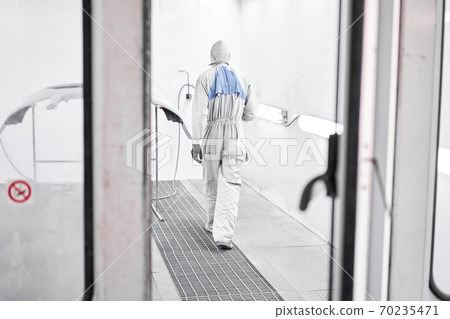 Worker painting parts of the car in special painting chamber, wearing costume and protective gear. Car service station. Repairing car body work after the accident by working sanding primer before 70235471