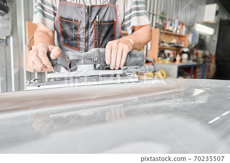 The mechanic works with a grinding tool. Sanding of car elements. Garage painting car service. Repairing car section after the accident. The mechanic works with a grinding tool. Sanding of car elements. Garage painting car service. Repairing car section after the accident. 70235507