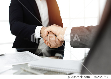 Unknown diverse business people are shaking hands finishing contract signing in sunny office, close-up. Business handshake concept 70235957