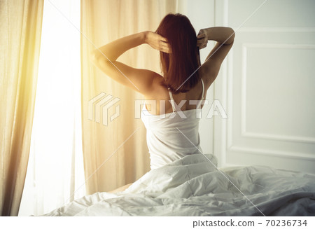 Woman stretching in bed after waking up, back view, entering a day happy and relaxed after good night sleep. Good morning and new day for brunette. Concept of Weekend, holidays 70236734