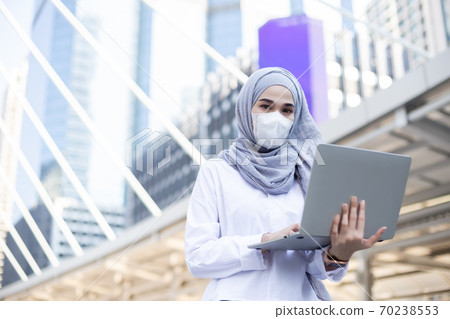 Asian muslim businesswoman wearing medical mask working with laptop. 70238553