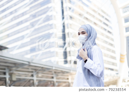 portrait young muslim woman wearing medical mask standing street side in city. 70238554
