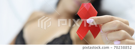 Woman is holding red ribbon while lying on t bed. 70238852