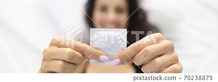 Woman holding condom while lying in bed. Woman holding condom while lying in bed. 70238875