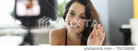 Woman lies on the bed in bra and records a video on camera and waves her hand in greeting Woman lies on the bed in bra and records a video on camera and waves her hand in greeting 70238898