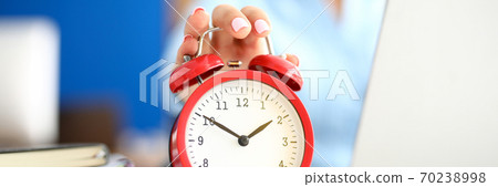 Woman in office holds a hand on red alarm clock. Woman in office holds a hand on red alarm clock. 70238998