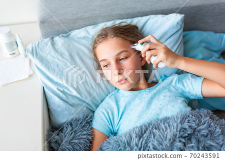 Sick teenage little girl with high fever and headache laying in bed checking her temperature 70243591